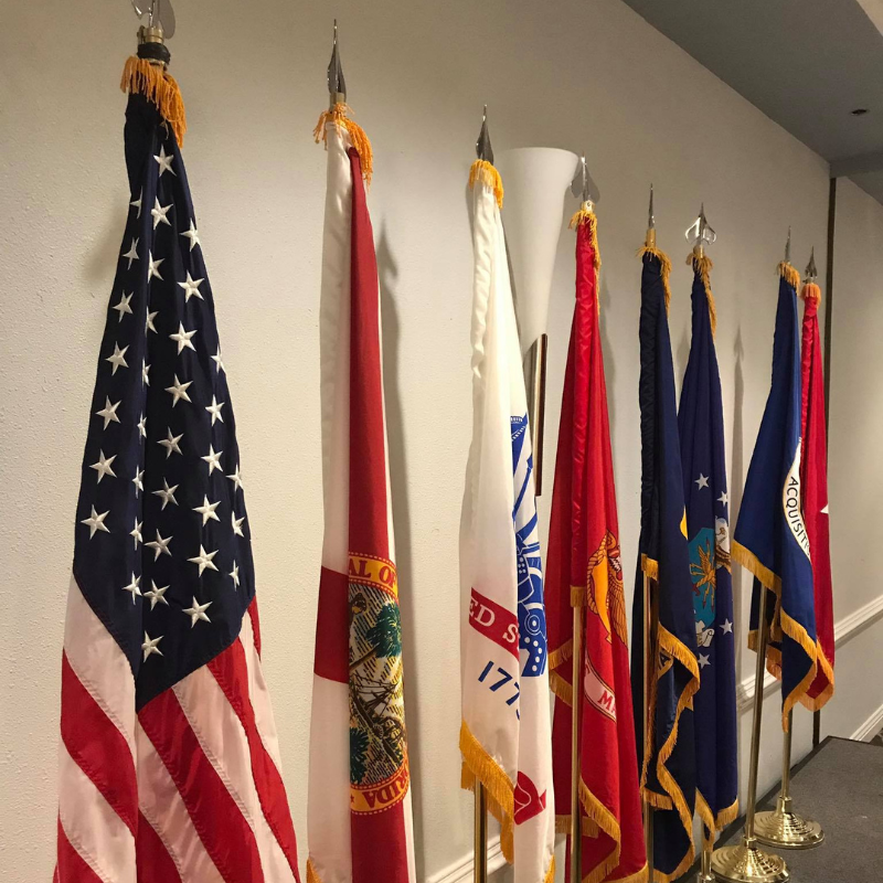 American and various American State and military flags on small flagpoles inside of an event space.